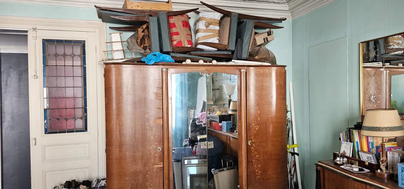 Grande armoire ancienne à miroirs, chaises et paquets empilés sur le dessus, porte vitrée à vitrail