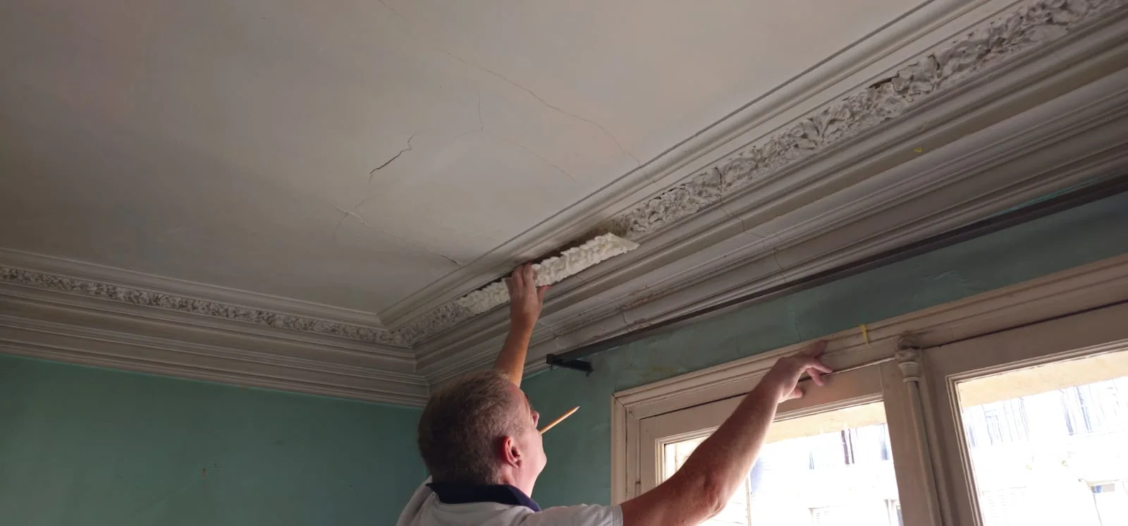 Un artisan repose un élément de corniche en plâtre au plafond d'un appartement ancien
