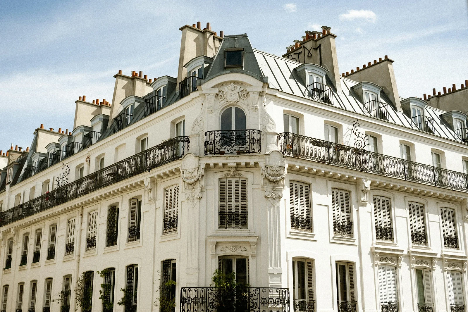 Façade parisienne blanche à toit mansardé et garde-corps en fer forgé