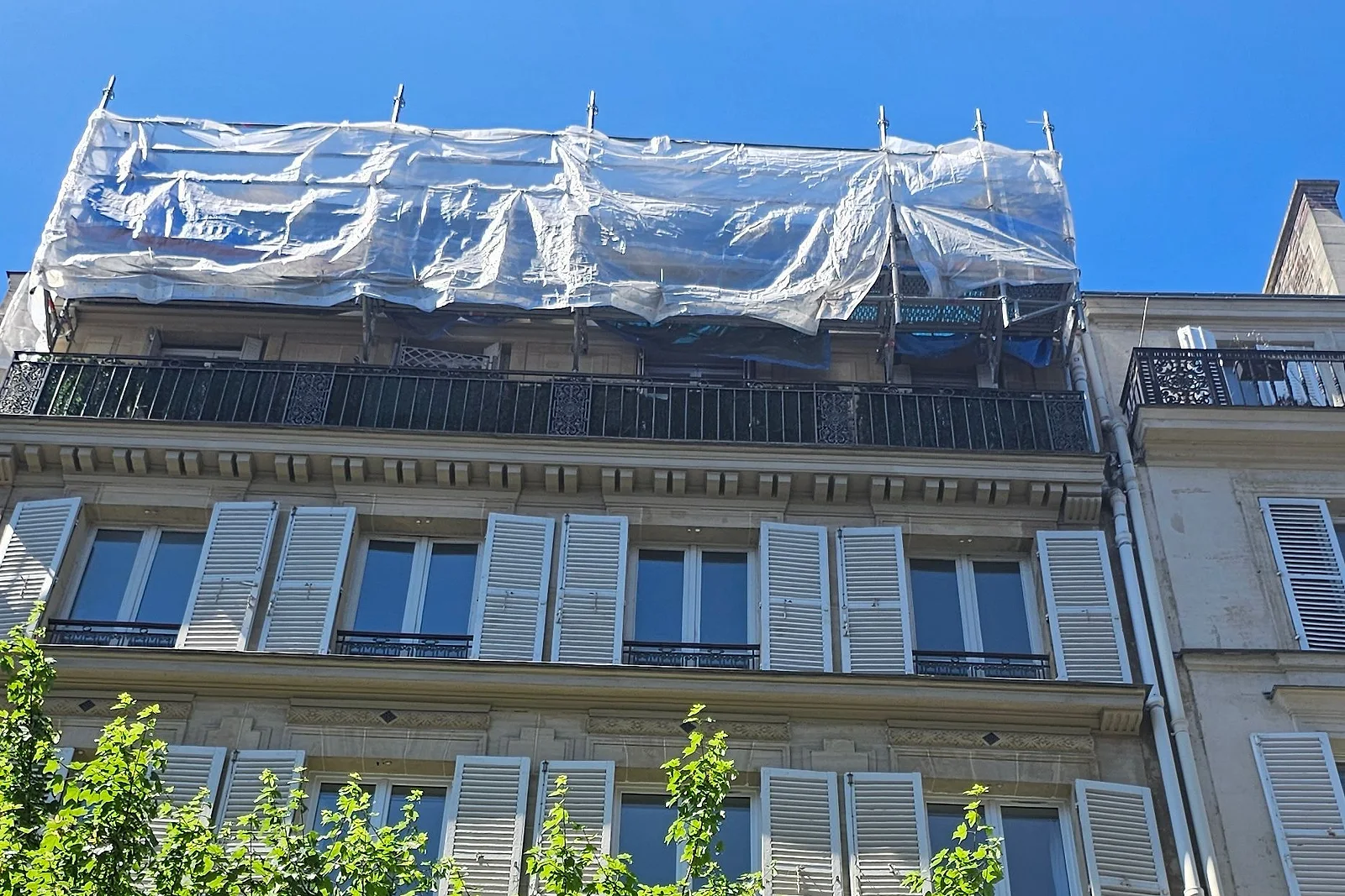 Immeuble ancien aux volets blancs, toiture en rénovation sous bâche