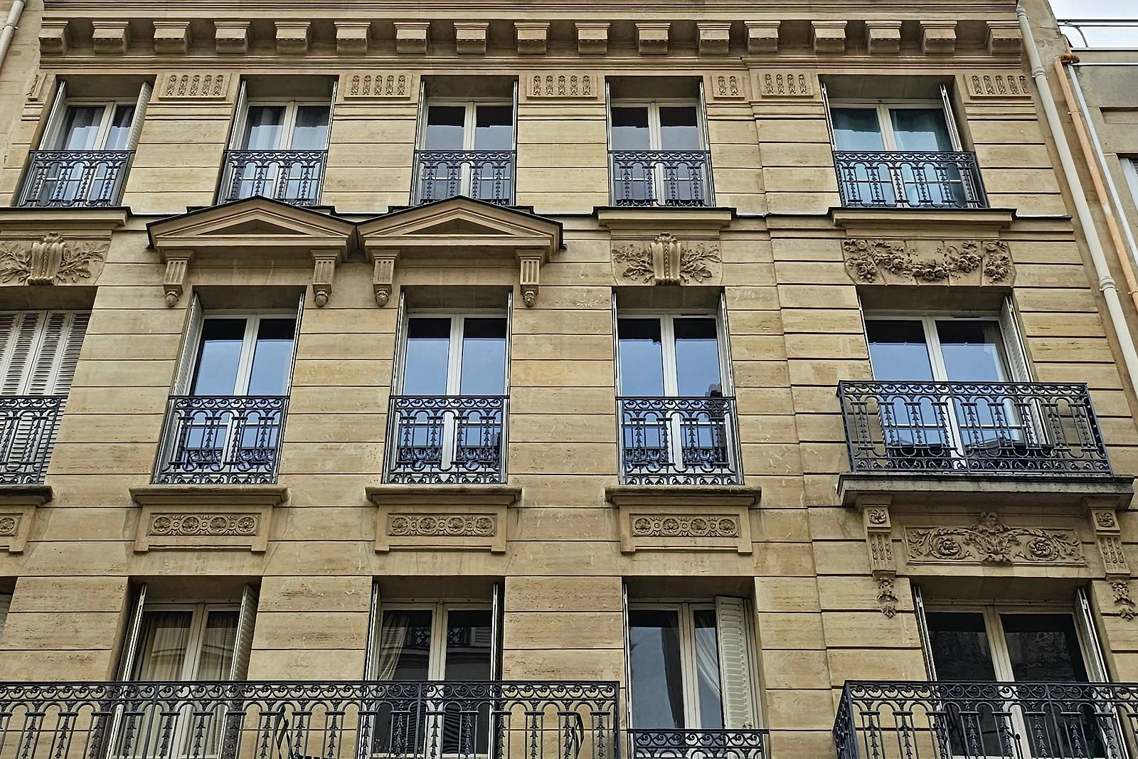 Façade d'immeuble en pierre de taille, frontons sculptés et balcons en fer forgé