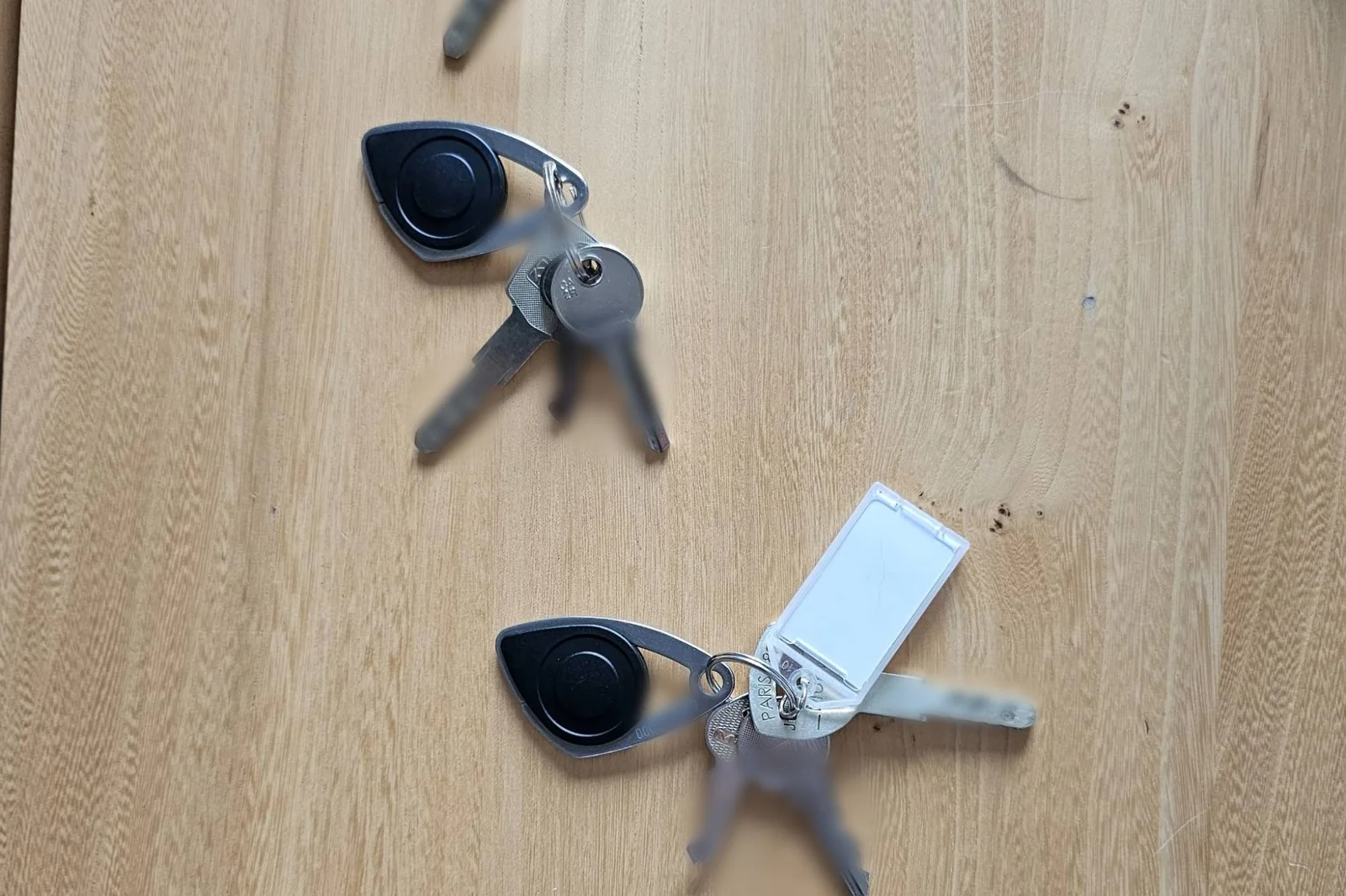 Deux trousseaux de clés et leurs badges d'accès posés à distance l'un de l'autre sur une table en bois